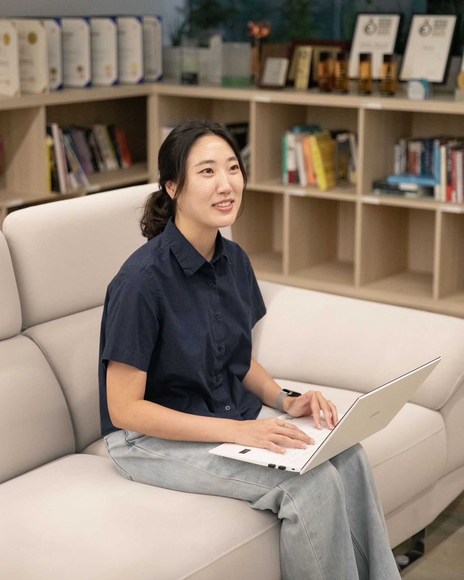 허윤정 그룹장이 트로피 선반 앞 소파에서 노트북으로 업무를 보고 있다