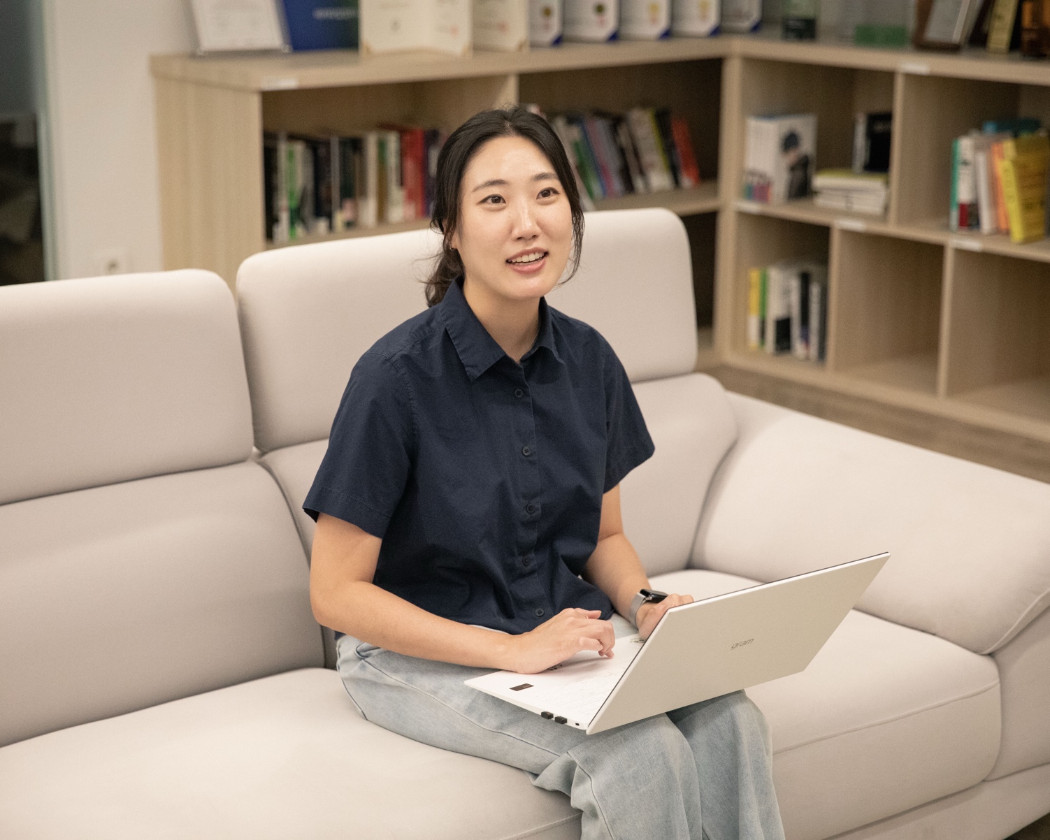 허윤정 그룹장이 트로피 선반 앞에서 노트북을 두고 웃으며 이야기하고 있다